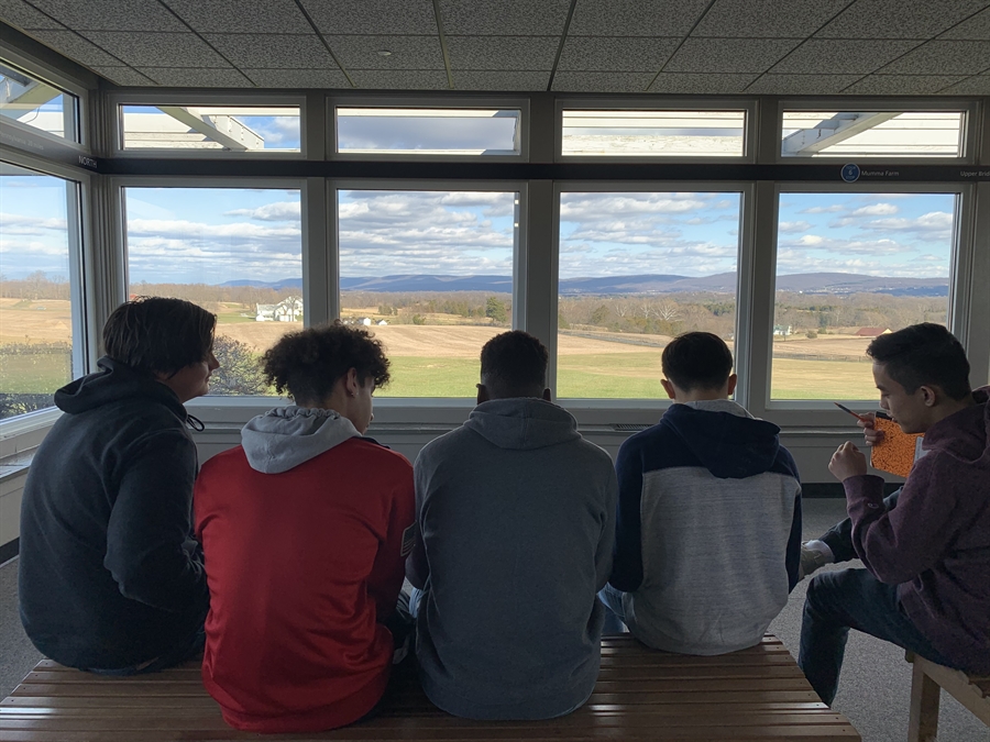 5 students sit on a bench looking out a window