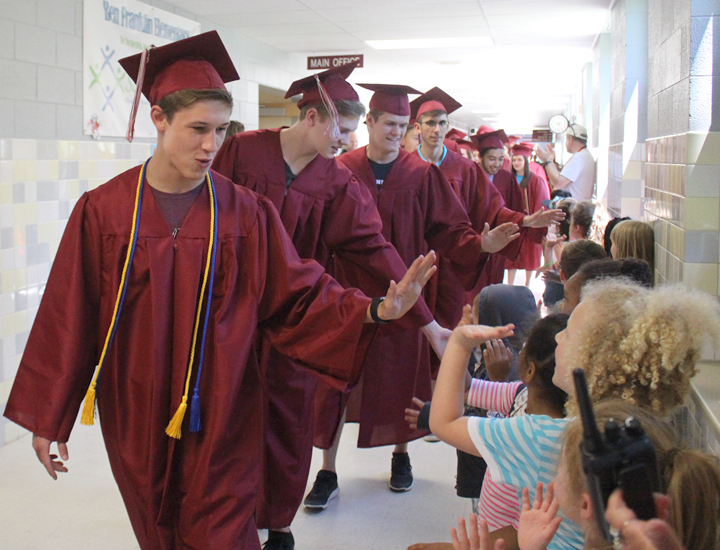 high school seniors in graduation attire parading past elementary students